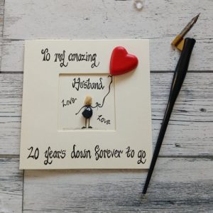 20th wedding anniversary card for husband, Handmade pebble art card, To my amazing husband, 20 years down forever to go. Male pebble figure holding a red heart shaped concrete balloon