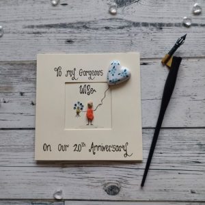 Handmade pebble art 20th wedding card for wife, handwritten using black ink, To my gorgeous wife, on our 20th Anniversary, female pebble figure holding a bunch of flowers a handpainted heart shape balloon. Created on cream card.