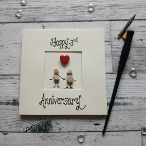Luxury anniversary card for any anniversary, a pair of pebble figures holding hands, above the couple a red heart. Created on cream card