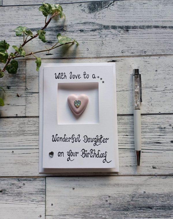 With love to a wonderful Daughter on your Birthday written onto a triple-fold white card with a small pink concrete heart with a sparkly gem in the middle