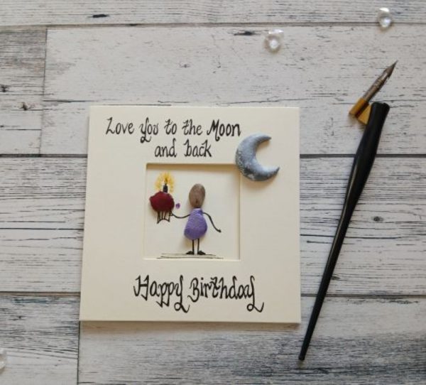 Happy Birthday card for the one you love, handmade pebble art card, Love you to the moon and back, Happy Birthday. Female pebble figure holding a cake and placed in the corner of the card a handpainted moon shaped pebble. Created on cream card.
