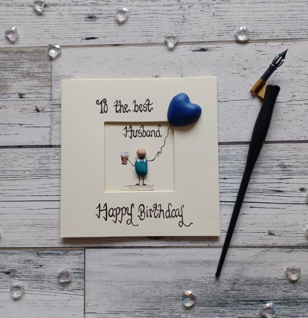 Birthday card for husband, handwritten in black ink, to the best husband Happy Birthday, handmade pebble art birthday card. Male pebble figure holding a beer and a blue heart shape balloon. Created on cream card.