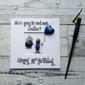 90th birthday card for him, a perfect card for a grandad or dad. Handmade pebble art card. Handwritten using black ink, We're going need more, Happy 90th birthday. Male pebble figure holding a big cake a blue heart balloon. Created on white card.