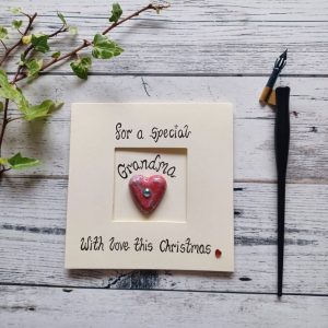 Handmade Christmas card for Grandma, handwritten using black ink, For a special Grandma, With love this Christmas. Placed in the centre of the card red heart shaped pebble. Created on cream card.