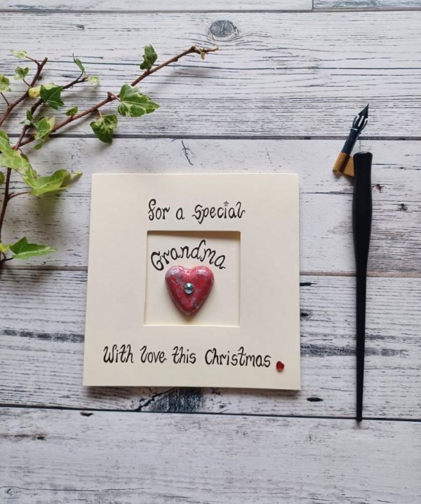 Handmade Christmas card for Grandma, handwritten using black ink, For a special Grandma, With love this Christmas. Placed in the centre of the card red heart shaped pebble. Created on cream card.