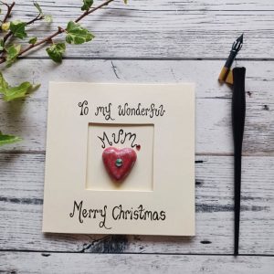 Handmade Christmas card for Mum, handwritten using black ink, To my wonderful Mum, Merry Christmas. Placed in the centre of the card red heart shaped pebble. Created on cream card.