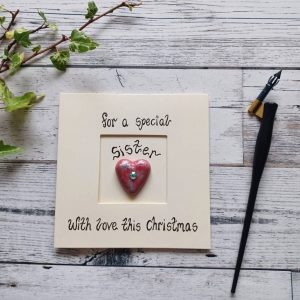 Handmade Christmas card for Sister, handwritten using black ink, For a special Sister, With love this Christmas. Placed in the centre of the card red heart shaped pebble. Created on cream card.