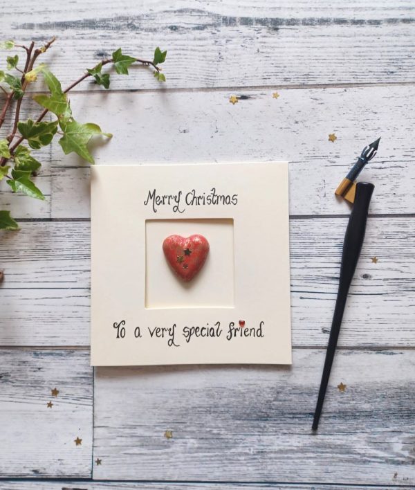 Handmade Christmas card for special friend, handwritten using black ink, Merry Christmas, To a very special friend. Placed in the centre of the card red heart shaped pebble. Created on cream card.