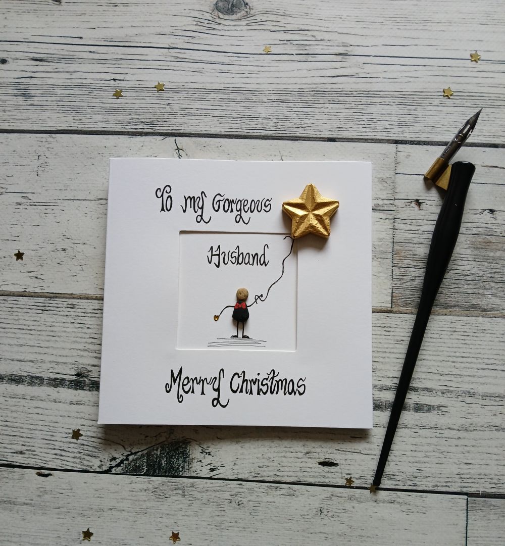 Christmas-card-for-husband-Husband-christmas-card-2 Handmade Christmas card for husband. Handwritten using black ink, To my gorgeous husband, Merry Christmas. Male pebble figure holding a gold star balloon. Created on white card.