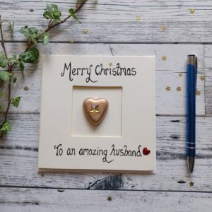 Handmade Christmas card for Husband, handwritten using black ink, Merry Christmas, To an amazing Husband. Placed in the centre of the card gold heart shaped pebble. Created on cream card.