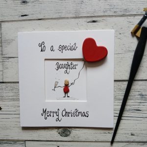 Handmade Christmas card for daughter. Handwritten using black ink, To a special daughter, Merry Christmas. female pebble figure holding a red heart balloon and a glass of champagne. Created on white card.