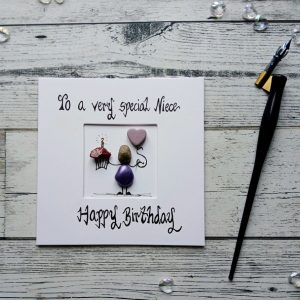 Handmade birthday card for niece, handwritten using black ink, To a very special Niece, Happy Birthday. Female pebble figure holding a cake and a pink heart shape balloon. Created on white card.