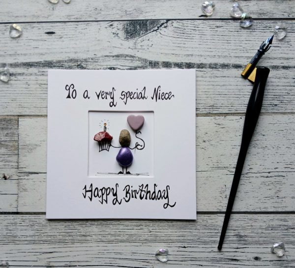 Handmade birthday card for niece, handwritten using black ink, To a very special Niece, Happy Birthday. Female pebble figure holding a cake and a pink heart shape balloon. Created on white card.