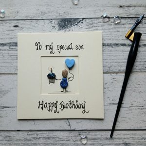 Handmade birthday card for son, handwritten using black ink, To my special Son, Happy Birthday. Male pebble figure holding a cake and a blue heart shape balloon. Created on cream card.